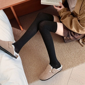 Detailed knit texture of black over-the-knee socks paired with stylish suede mules