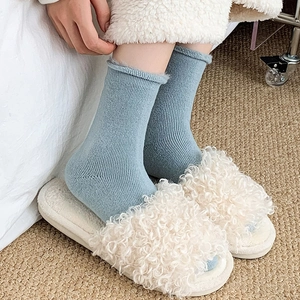 Close-up of light blue ribbed winter socks paired with plush cream faux fur slippers