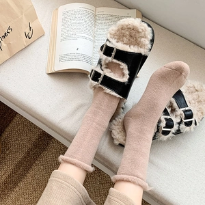 Close-up of pink knitted crew socks paired with black fleece-lined buckle slippers at home