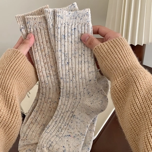 Close-up of thick beige wool blend ribbed socks with colorful flecks held by hand