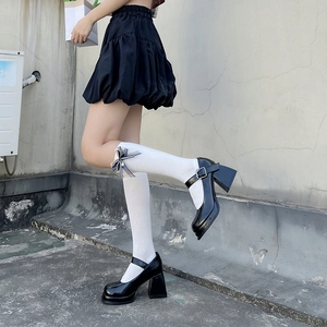 Detail of white knee-high socks with black ribbon bow and patent leather Mary Jane shoes
