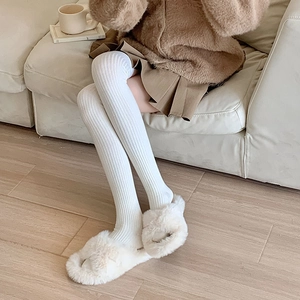 Close-up of white ribbed knit over-the-knee socks paired with plush slippers