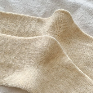Detailed macro shot of warm off-white knit thigh-high socks with thick wool texture