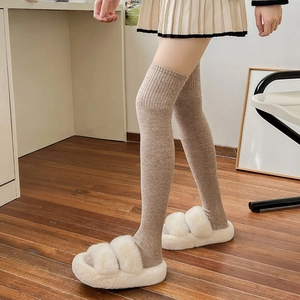 Detail of oatmeal over-knee knit socks and ivory faux fur slippers on wooden floor