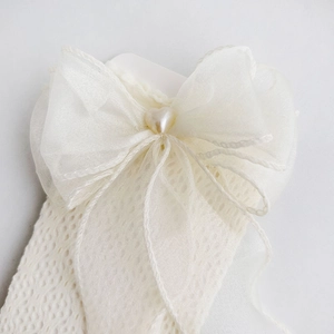 Detail of white lace mesh sock featuring a large organza bow and heart pearl charm