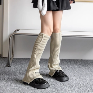 Detail of cream white ribbed knit leg warmers with stitched BJNAR label over black shoes