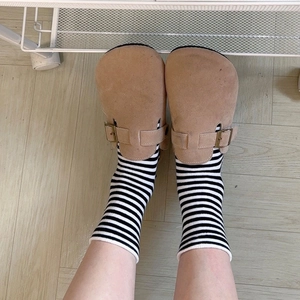 Detail view of khaki suede mule clogs with metal buckle strap worn with striped socks
