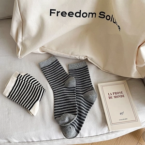 Flat lay di calze a righe in cotone su tessuto beige con libro e borsa in tela decorativa