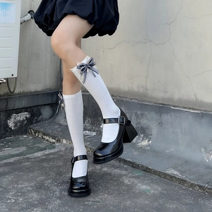 Detail of white knee-high socks with black bow and platform Mary Jane shoes