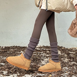 Détail de jambières en maille gris foncé portées sur des bottes classiques en daim camel