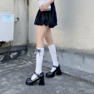 Detail of white knee-high socks with delicate bow accent and black Mary Jane platform shoes