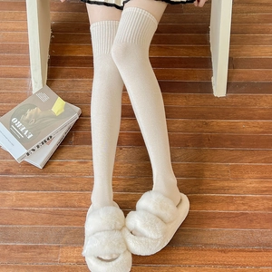Detail of cream over-the-knee knit wool socks paired with plush white slippers on wood floor