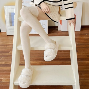 Detailed knit texture of cream white over-knee wool socks worn with plush platform slippers