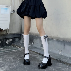Detail of white lace knee-high socks with dark bows and pearl accents for JK style