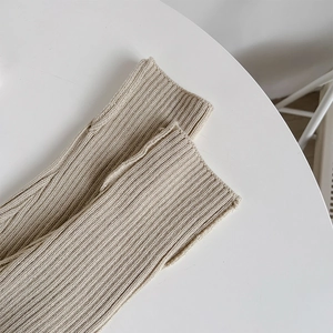 Close-up of beige ribbed knit leg warmers featuring thumb holes on a white surface