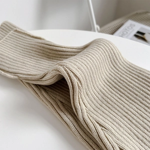 Close-up of thick beige ribbed knit leg warmers with detailed texture on white surface