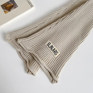 Detailed texture of beige cable knit leg warmers with a stylish rectangular woven label