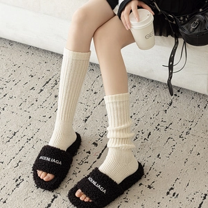 Détail de sandales en fausse fourrure noire brodée et chaussettes en maille beige