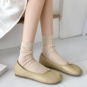 Dettaglio di scarpe tabi verde oliva con decoro a sfera dorata e calzini beige in maglia