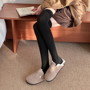 Thick over-knee socks styled with warm taupe suede clogs in a cozy indoor setting