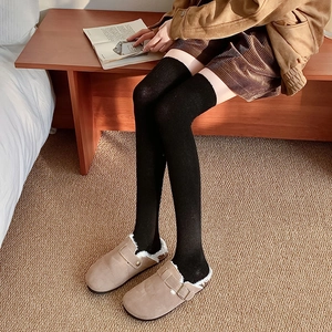 Detail of black over-the-knee warm socks styled with fur-lined suede mule slippers