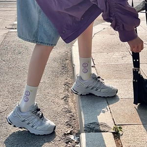 Dettaglio di sneaker grigie con logo FUYAXING e calze bianche con faccine viola