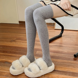 Thick grey knitted over-knee wool socks paired with warm plush slippers on wood floor