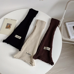 Close-up of ribbed knit leg warmers in black, beige, and brown with woven labels