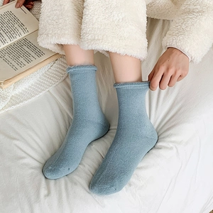 Close-up of Morandi blue ribbed knit socks with rolled cuffs on a cozy white bed