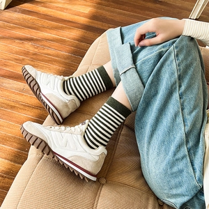 Sneaker retrò crema con logo N e calzini a righe su un pavimento in legno caldo