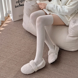 Detail of white knitted over-knee socks with ribbed texture and plush slip-on shoes