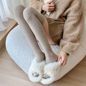 Close-up of khaki knit over-the-knee socks with vertical ribbed texture and fuzzy slippers