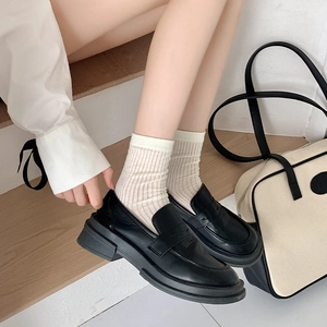Detail von matten Leder-Loafers in Schwarz mit creme-gestreiften Socken auf Holzstufen