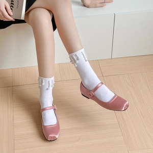 Gros plan de Mary Janes en satin rose avec chaussettes blanches ornées de perles