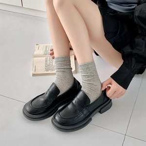 Detail von schwarzen Plateau-Loafern kombiniert mit grauen gerippten Socken für einen Preppy-Look