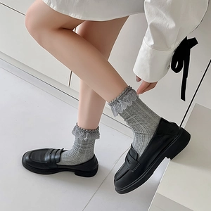 Detail of grey knitted socks with delicate lace trim paired with black loafers