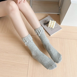 Détail de chaussettes en maille grise avec élégants glands de perles blanches