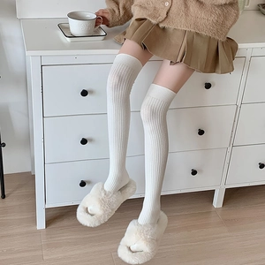 Detail of white ribbed knit over-knee socks paired with plush slippers in a home setting