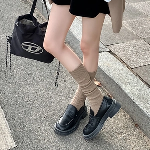 Detalle de calcetines de punto marrón con mocasines negros de plataforma en cuero