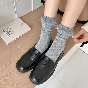 Detail of grey cable knit socks featuring elegant lace trim paired with black loafers