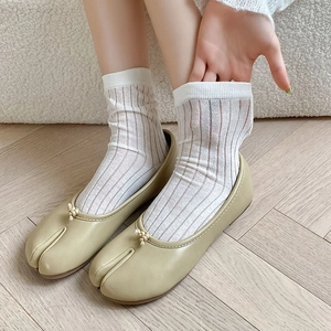 Dettaglio di ballerine Tabi color crema con fiocco abbinate a calze bianche a righe