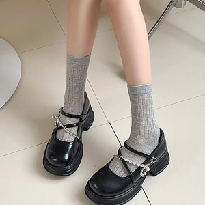 Dettaglio di scarpe Mary Jane nere con plateau, catena di perle e calze grigie