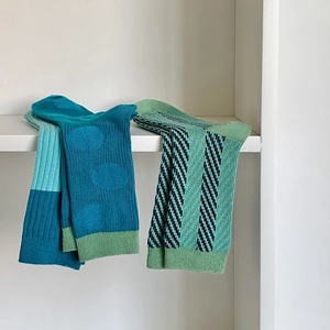 Detailed knit of peacock blue polka dot and green striped crew socks on display