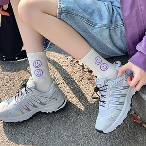 Dettaglio di calzini bianchi in cotone con smiley viola e testo hi indossati con scarpe