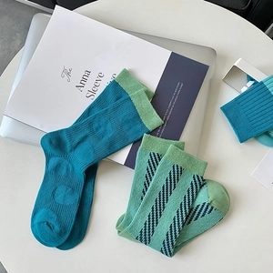 Detail of blue and green knit crew socks with diagonal stripes on a desk with a laptop