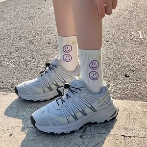 Dettaglio scarpa sportiva in mesh con allacciatura rapida e calzini smiley su asfalto