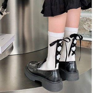 Détail de chaussettes mi-mollet blanches avec laçage arrière et nœud en ruban noir