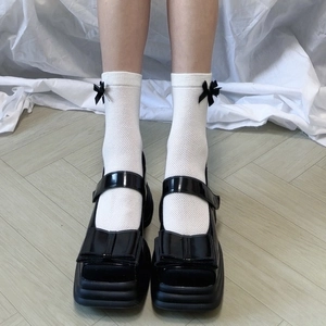 Dettaglio di calze a rete bianche con fiocchi neri e scarpe Mary Jane con plateau