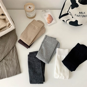 Flat lay of ribbed cotton mid-calf socks in six neutral colors with minimalist props