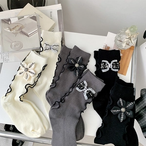 Detail of knit socks with wavy ruffled cuffs and branded ribbon bow flower accents
